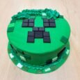 Round bright-green Minecraft Creeper cake with a raised charcoal pixel face, piped grass texture and green, mint and white block decorations