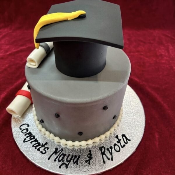 Silver-grey Graduation Day Cake with black mortarboard, yellow tassel, two diploma scrolls, black dot accents, white piped border and custom names