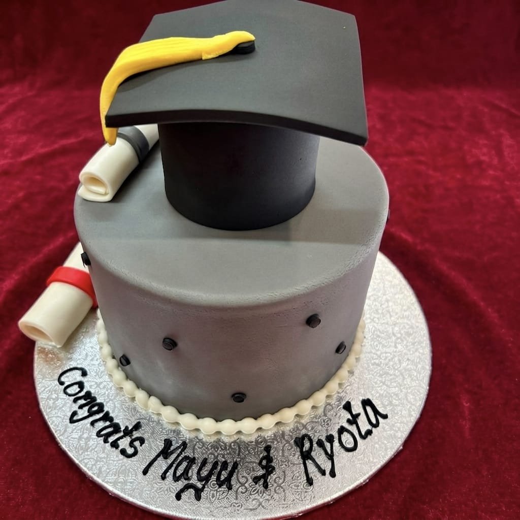 Silver-grey Graduation Day Cake with black mortarboard, yellow tassel, two diploma scrolls, black dot accents, white piped border and custom names