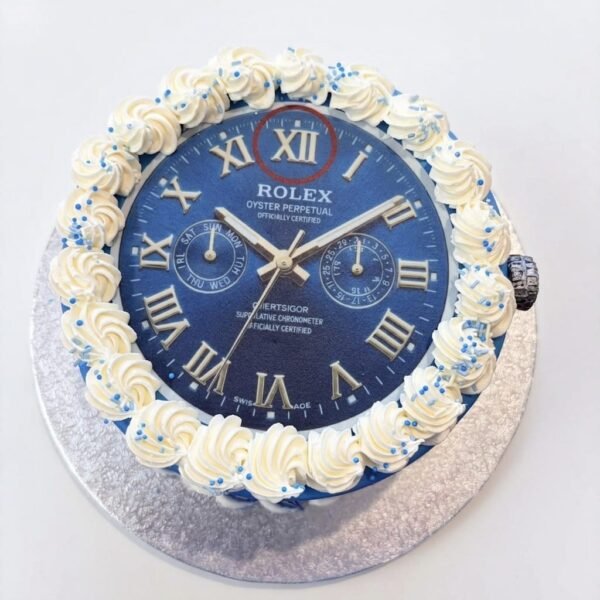 Blue Rolex chronograph watch face cake with silver Roman numerals, twin subdials, metallic hands, side crown and sprinkled rosette piping