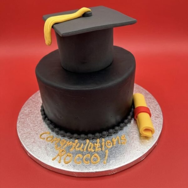 Black Graduation Day Cake with sculpted mortarboard, yellow tassel, rolled diploma, red band, black piped border and gold congratulations message