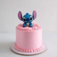 Disney Stitch pink rosette cake with smooth blush sides, matching piped borders and a blue character leaning over the top