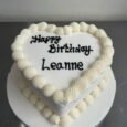 Classic white heart-shaped cake with smooth ivory icing, large shell-piped borders and a replaceable black celebration message
