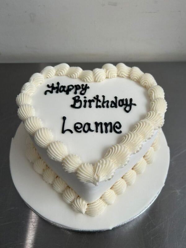 Classic white heart-shaped cake with smooth ivory icing, large shell-piped borders and a replaceable black celebration message