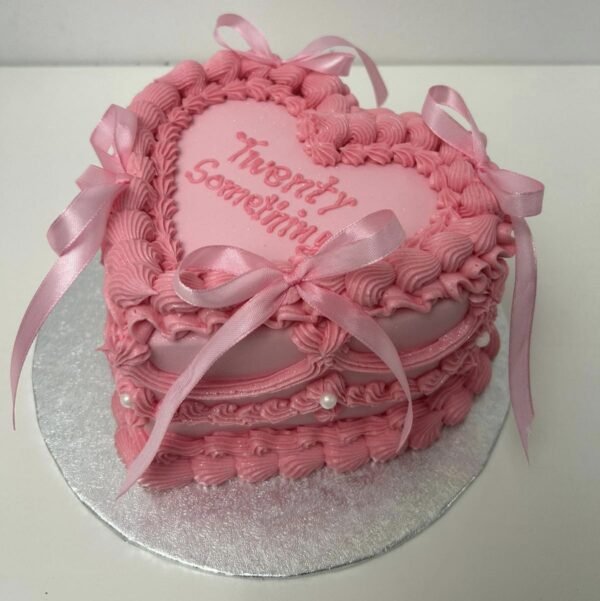 Blush pink vintage Lambeth heart cake with ornate layered piping, scalloped swags, pearl accents, satin ribbon bows and custom message