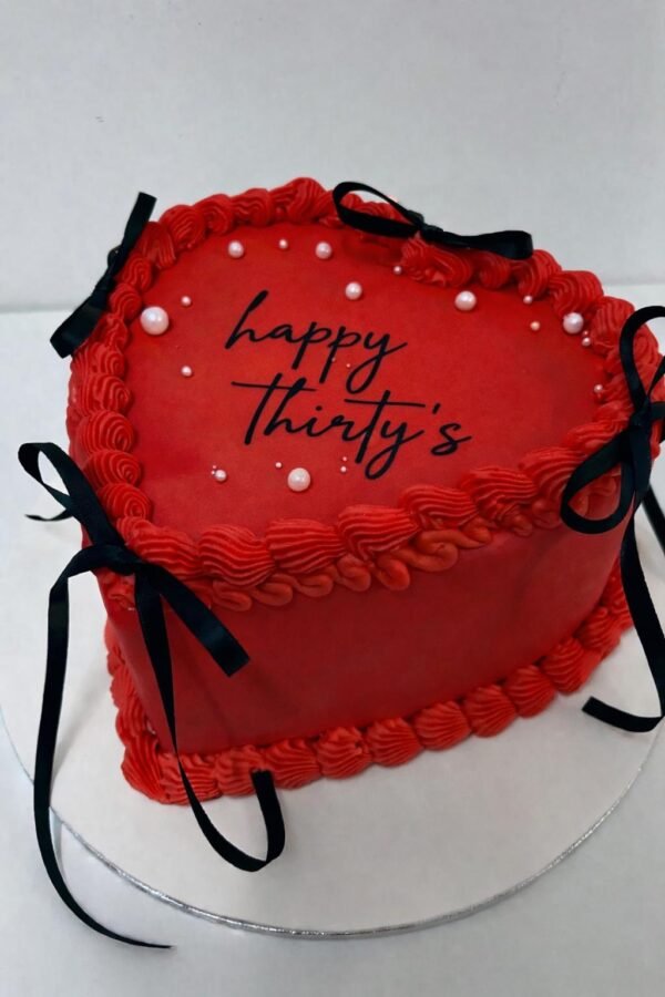 Red vintage heart cake with layered Lambeth piping, pearl accents, black ribbon bows and a custom centre message