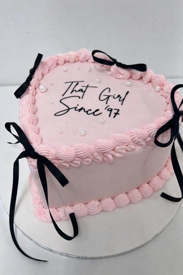 Pink vintage heart cake with Lambeth-style shell piping, pearl accents, black ribbon bows and a replaceable centre message
