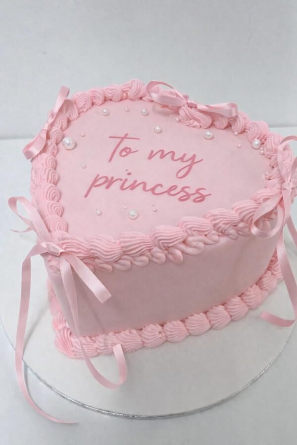 Pink vintage heart cake with matching shell piping, braided borders, satin ribbon bows, pearl-style decorations and custom centre message