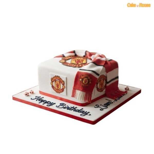 Square white Manchester United football cake with multiple club crests, red base trim and a realistic red, white and black team scarf