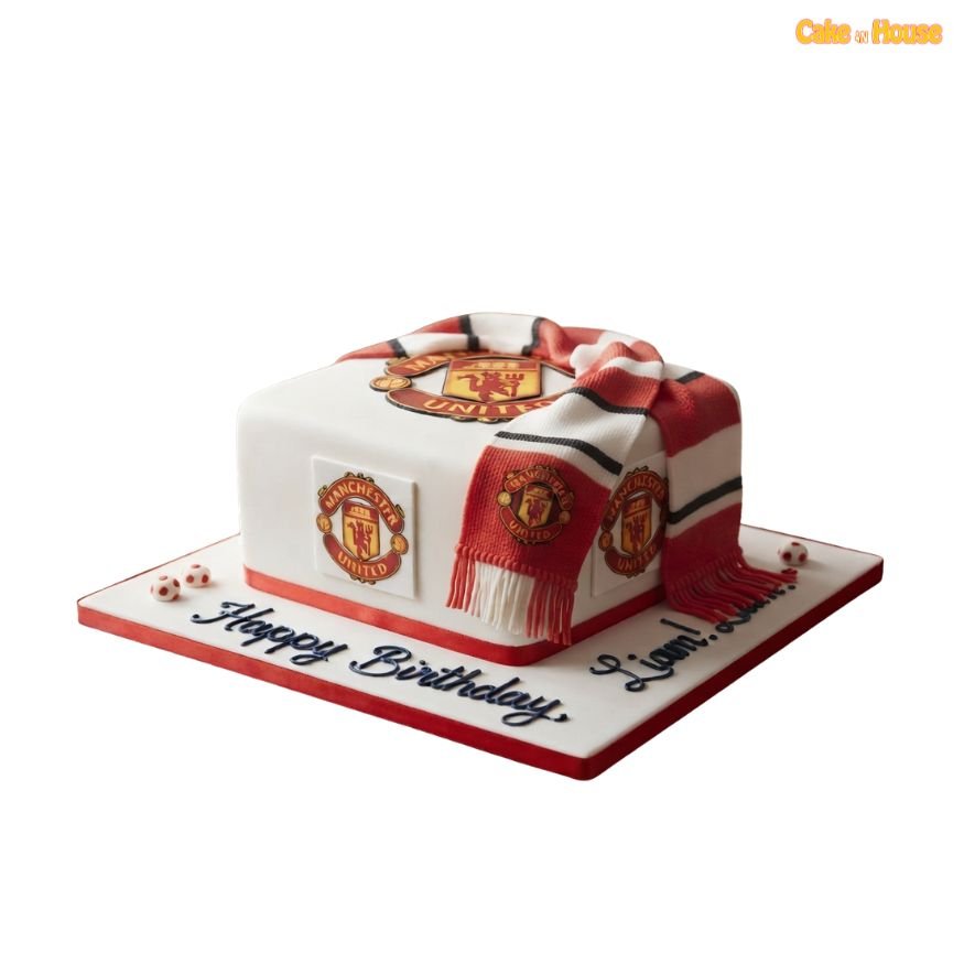 Square white Manchester United football cake with multiple club crests, red base trim and a realistic red, white and black team scarf