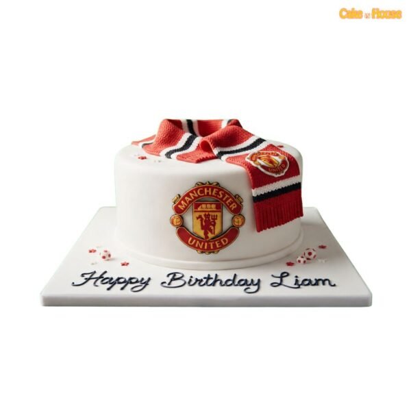 White round Manchester United football cake with a large club crest, red and black team scarf, miniature footballs and custom wording