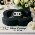 Black Chanel logo birthday cake with sculpted CC-style shape, white logo detail, gold accents and personalised birthday message
