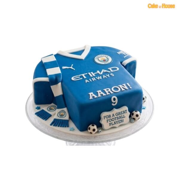 Sculpted blue Manchester City football shirt cake with white trim, club crest, matching scarf, miniature footballs and personalised details